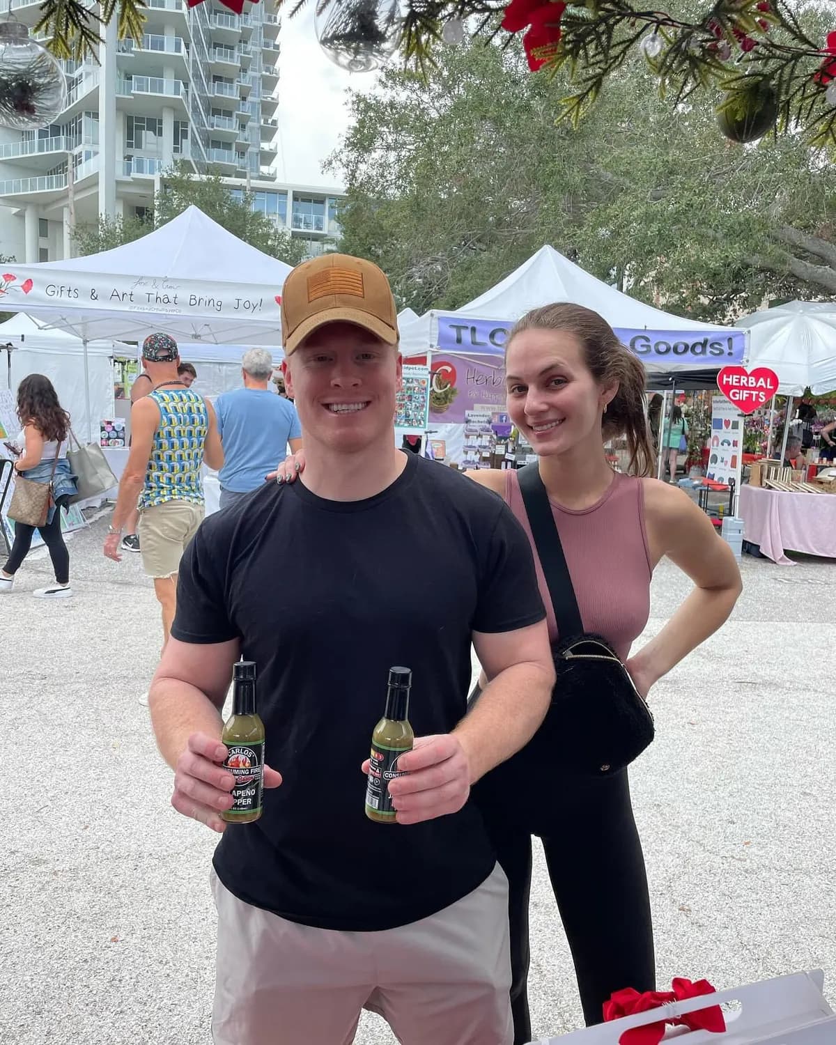 Couple each holding a Jalapeño Hot Sauce bottle at a holiday farmers market