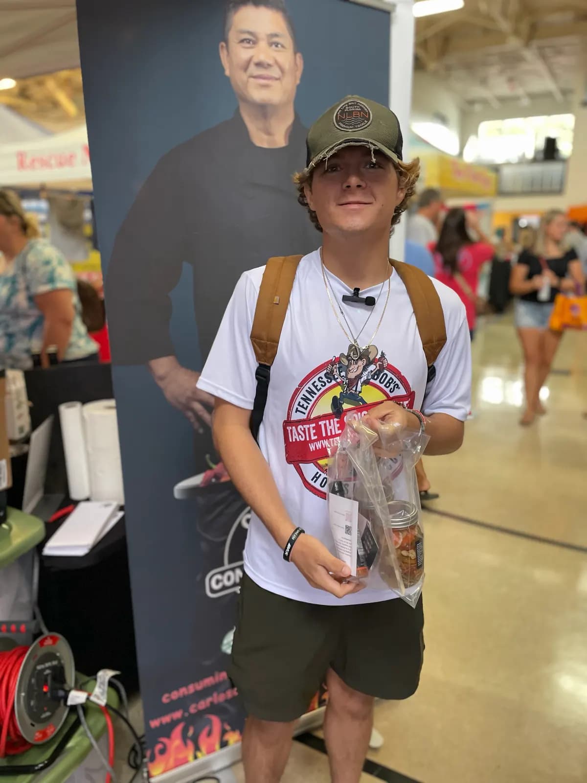 Young customer with a purchase in front of the Carlos' Consuming Fire Hot Sauce banner
