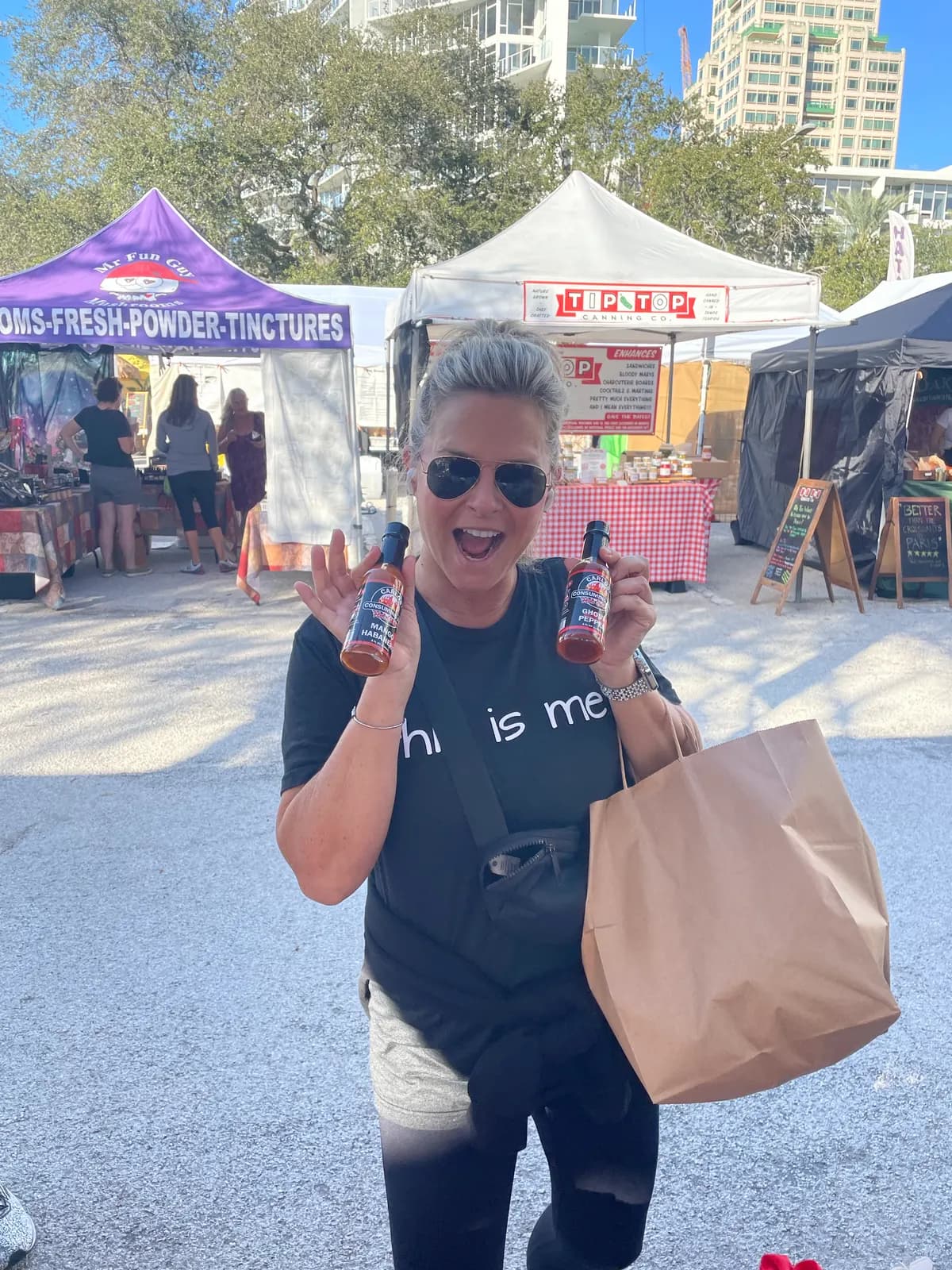 Fan holding up two Carlos' Consuming Fire Hot Sauce bottles at an outdoor farmers market