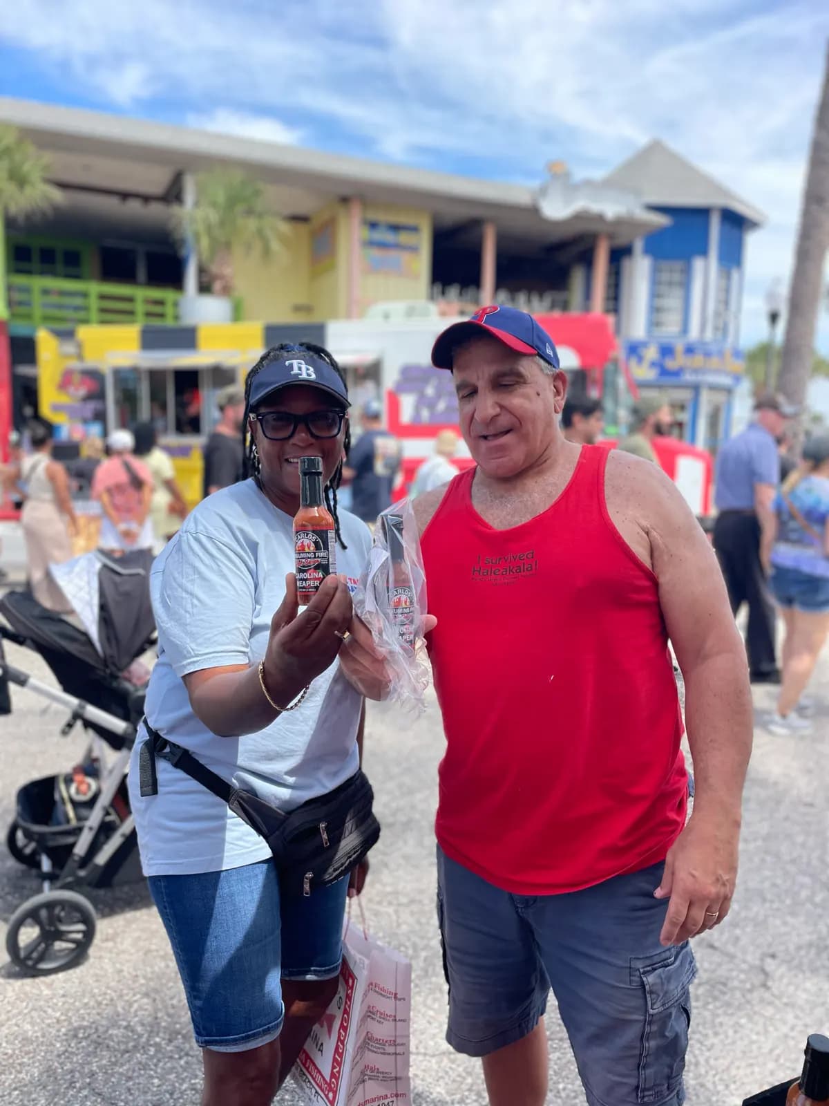 Two festival-goers holding up a sauce bottle and a bagged purchase