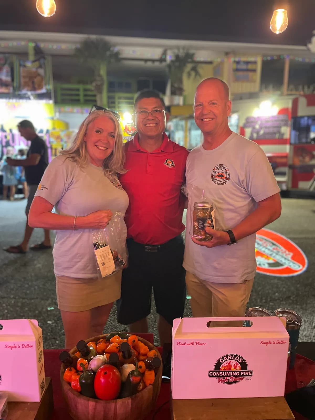 Carlos with two smiling customers holding a jar at the night festival booth