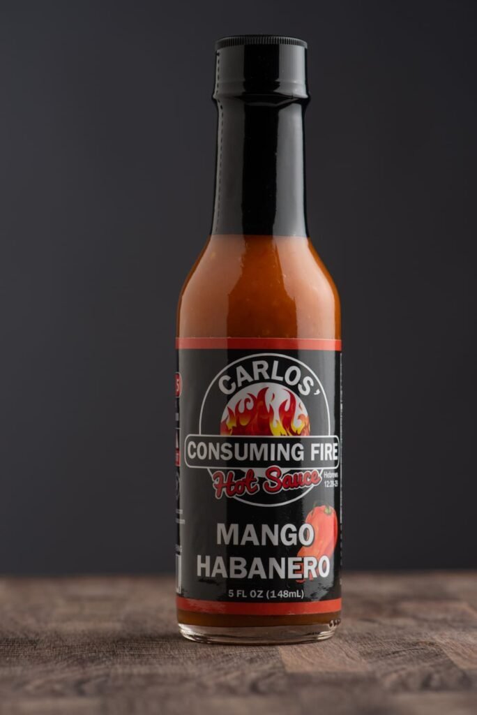 Front view of Carlos' Consuming Fire Hot Sauce Mango Habanero bottle, 5 FL OZ (148mL).