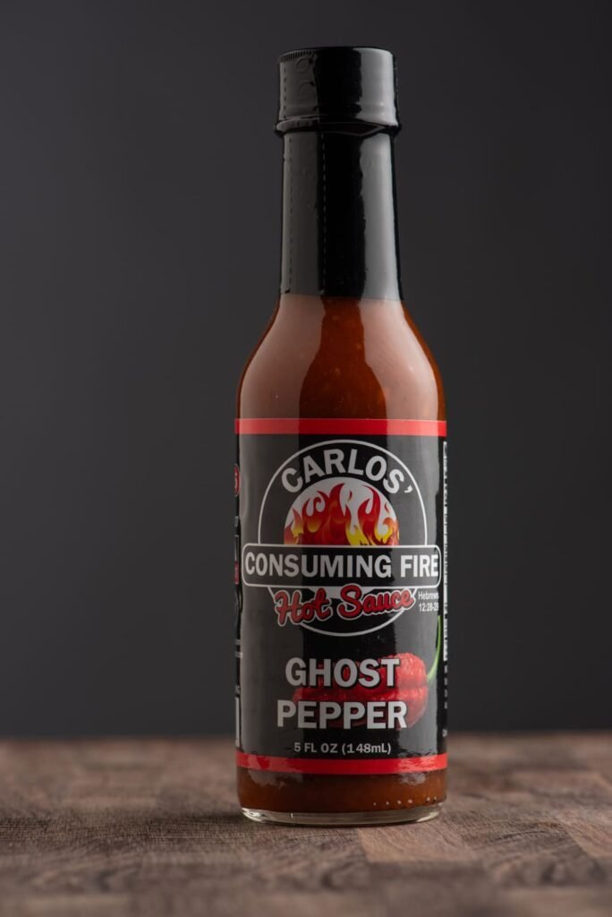 Front label of Carlos' Consuming Fire Hot Sauce Ghost Pepper bottle, 5 FL OZ (148mL).