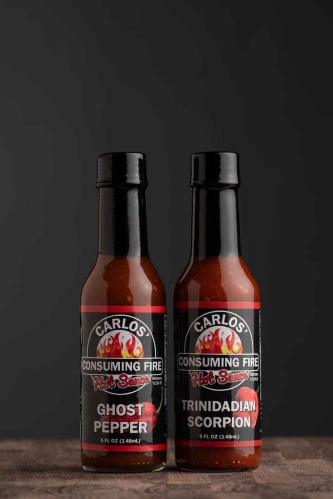 Carlos' Consuming Fire Hot Sauce, Smokin’ Hot Bundle: Ghost Pepper and Trinidadian Scorpion hot sauce bottles on a dark background.