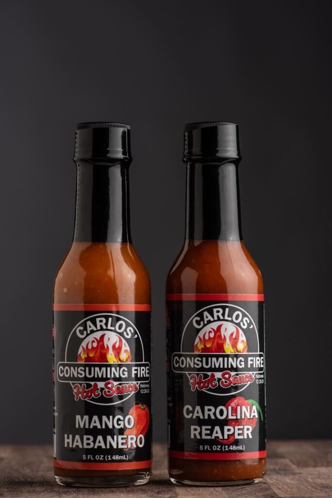 Carlos' Consuming Fire Hot Sauce Sweet Heat Bundle: Mango Habanero and Carolina Reaper hot sauce bottles on a dark background.