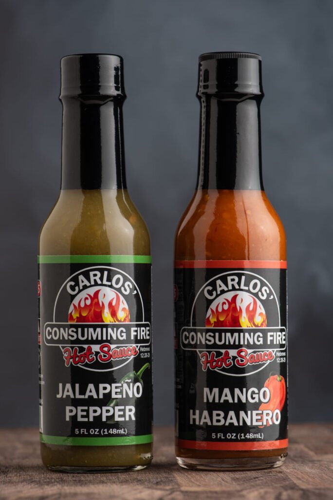Carlos' Consuming Fire Hot Sauce Twice as Nice Bundle: Jalapeño Pepper and Mango Habanero hot sauce bottles on a rustic wooden surface.
