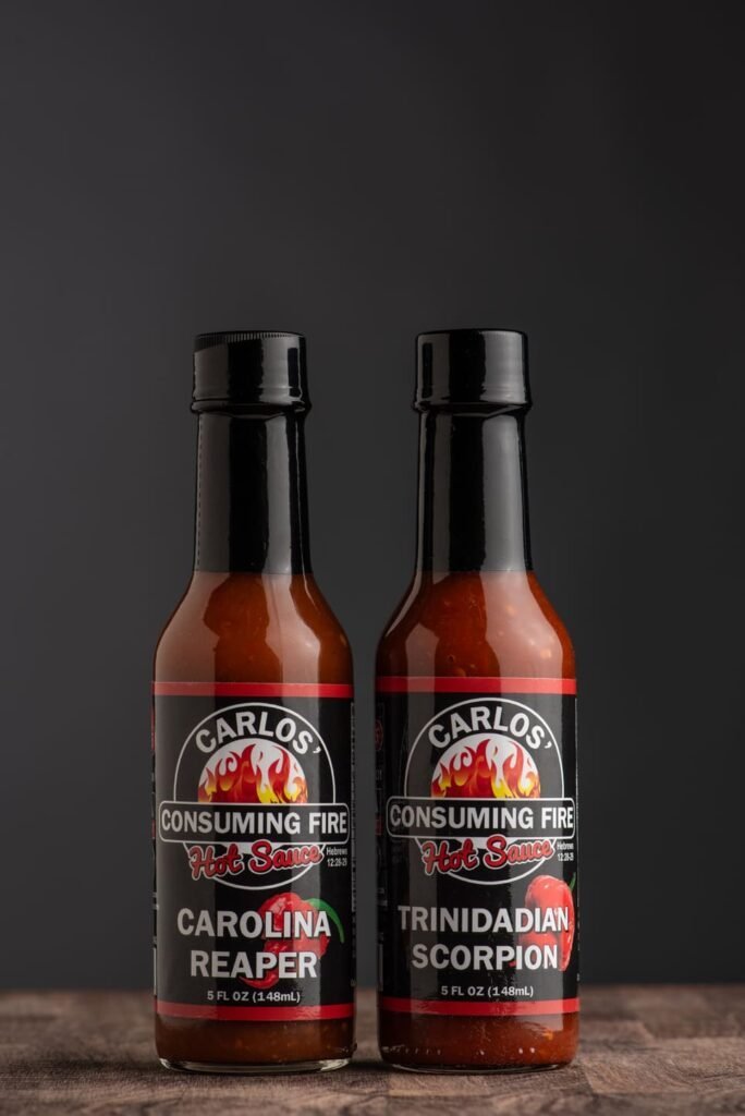 Carlos' Consuming Fire Hot Sauce Heat Lovers Bundle: Carolina Reaper and Trinidadian Scorpion hot sauce bottles on a dark background.