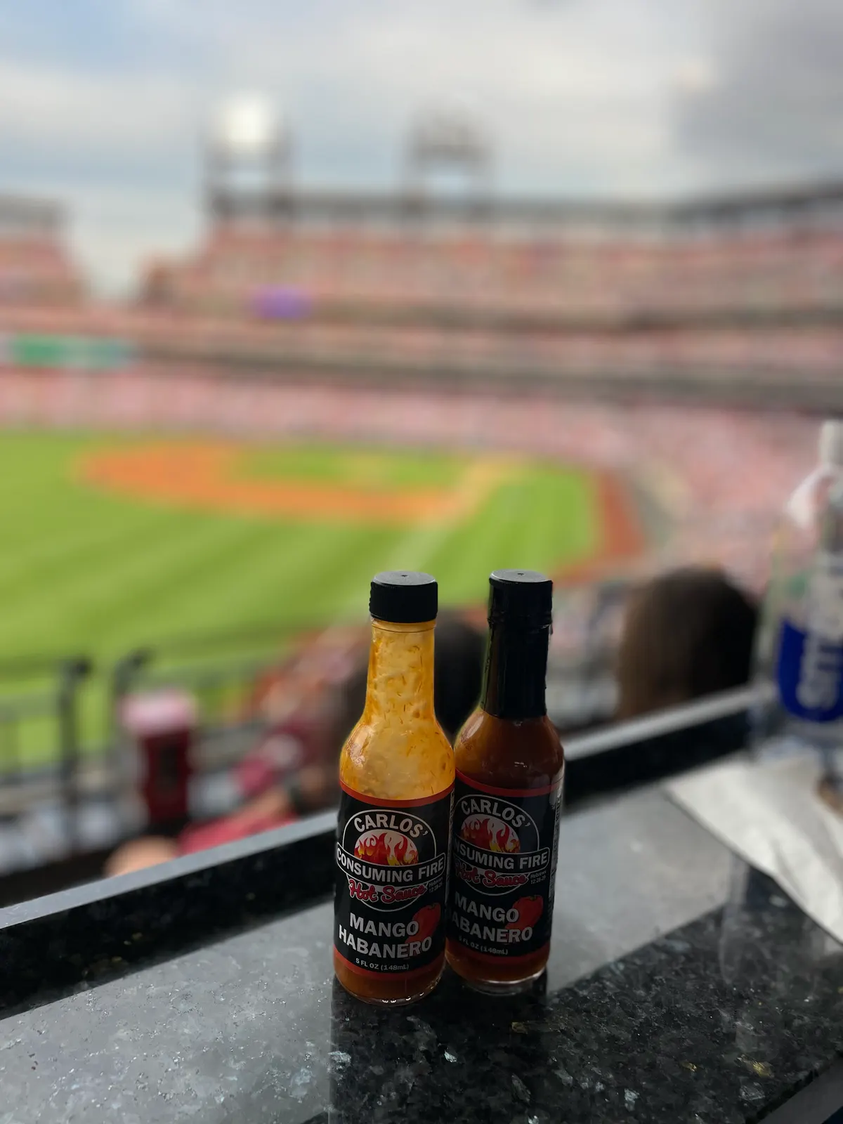 Two Mango Habanero Hot Sauce bottles on a stadium suite ledge above the ballpark field