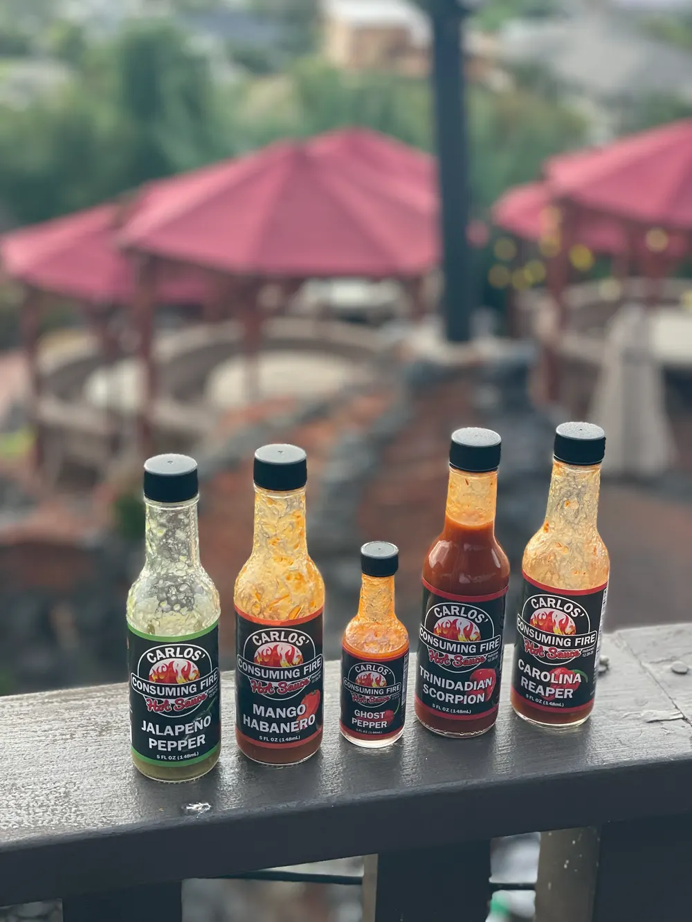 All five Carlos' Consuming Fire Hot Sauce bottles lined up outdoors
